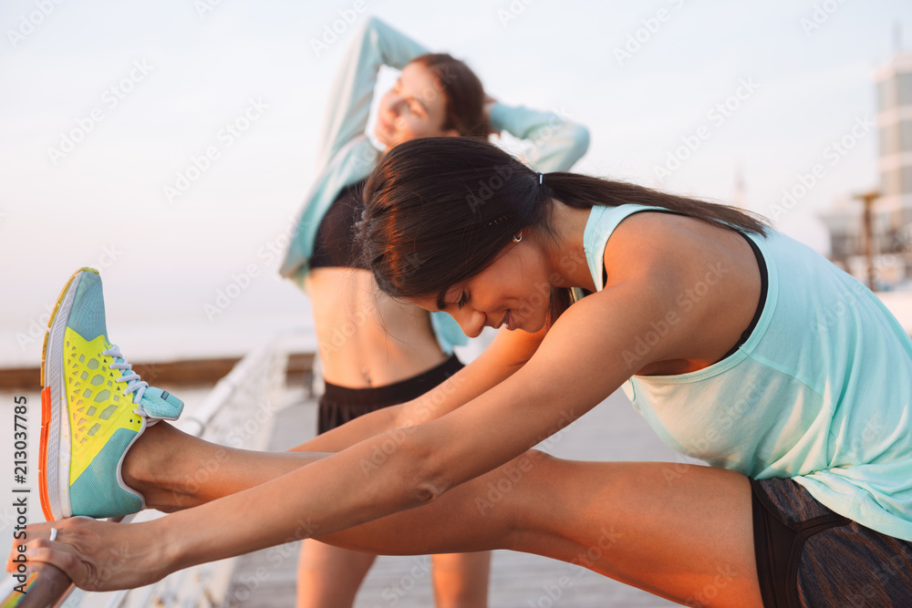 Young two sports women friends outdoors on the beach make sport exercises. Young two sports women friends outdoors on the beach make sport exercises.