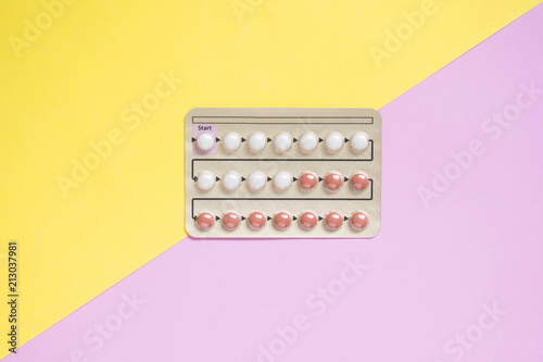 Oral contraceptive pills blister on yellow pink background. Hormones used to prevent pregnancy and treat other medical conditions, such as PCOS, endometriosis, amenorrhea or acne. Gynecology concept. photo