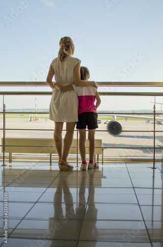 Fototapeta Naklejka Na Ścianę i Meble -  a girl with a child is standing near the window at the airport and waiting for the arrival of the aircraft