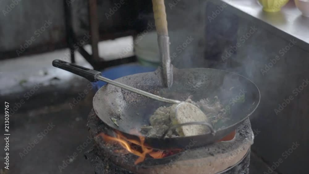 Slow motion shot of a man cooking with charcoal stove. Noodle dish in wok made on open fire. Street food in Chinatown of Bangkok, Thailand Slow motion shot of a man cooking with charcoal stove. Noodle dish in wok made on open fire. Street food in Chinatown of Bangkok, Thailand