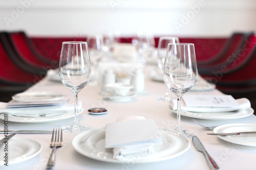 Perspective view of table set with white dishware and crystal clear wineglasses on white tablecloth