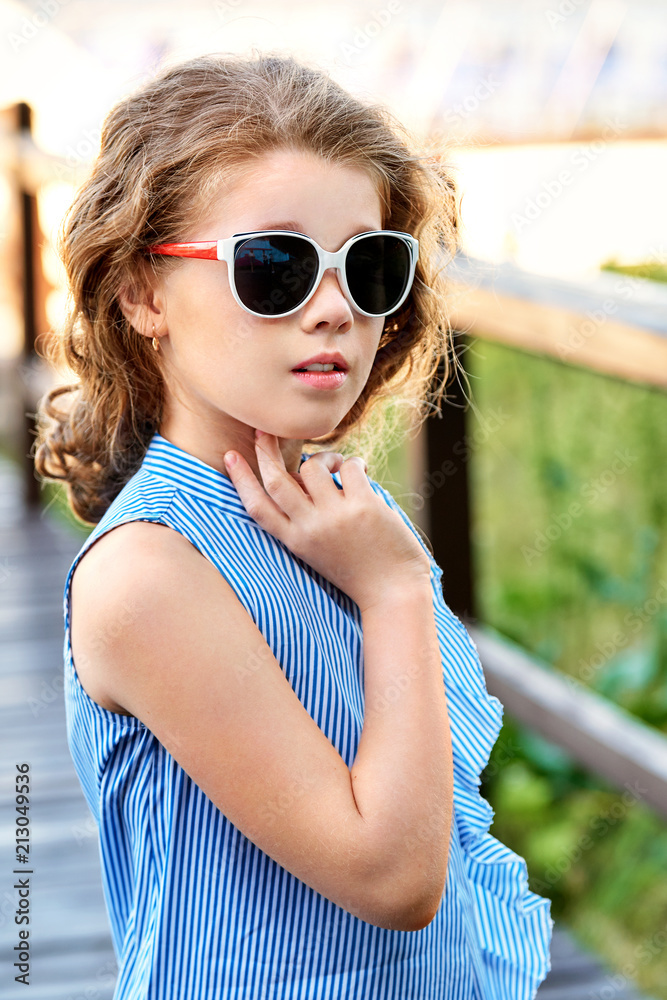Elegant child portrait. Little girl model wearing summer cool clothing,  sunglasses. Marine style, outdoors. Looking away. Fashion kid concept.  Stock Photo | Adobe Stock