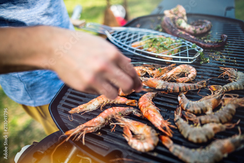 Unrecognizable man cooking seafood on a barbecue grill in the backyard. Close up.