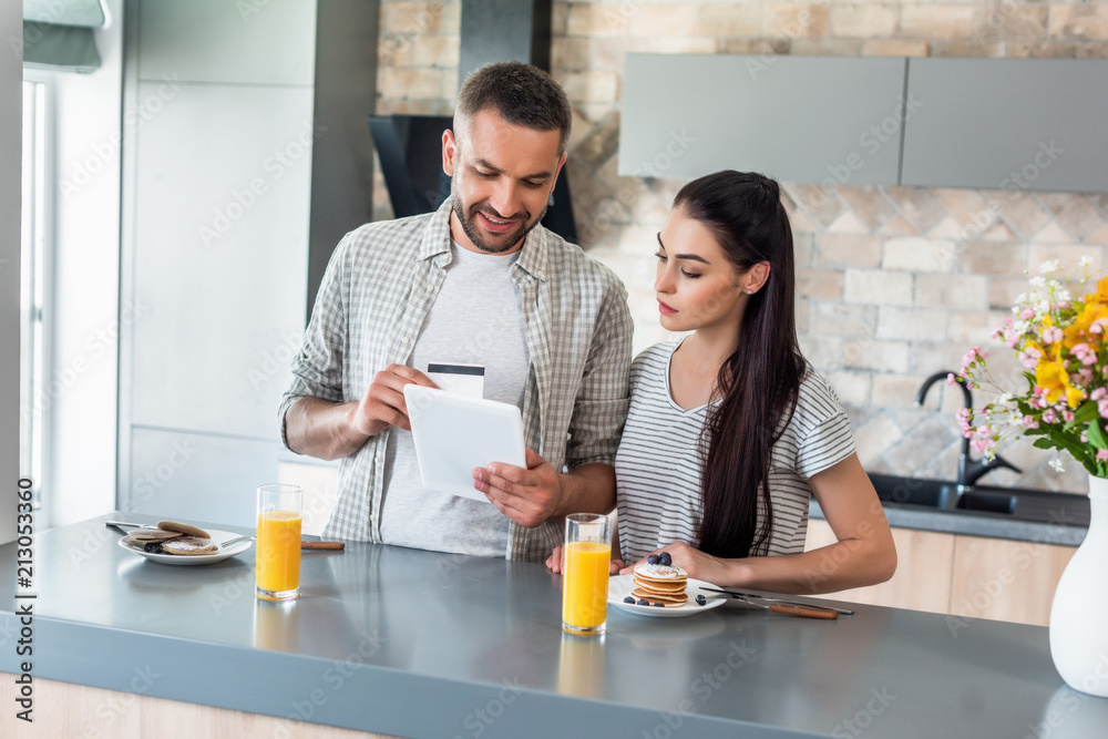 portrait of couple using tablet at counter with homemade breakfast in kitchen portrait of couple using tablet at counter with homemade breakfast in kitchen