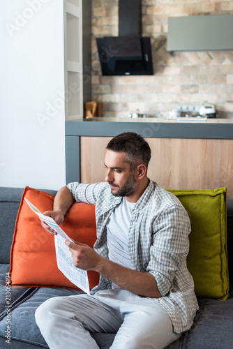 Tableau sur toile portrait of focused man reading newspaper on sofa at home