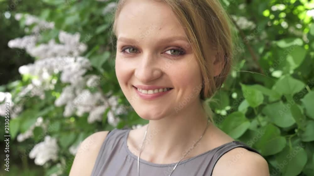 Young cute blond girl is watching at camera in park in daytime in summer, smiling Young cute blond girl is watching at camera in park in daytime in summer, smiling