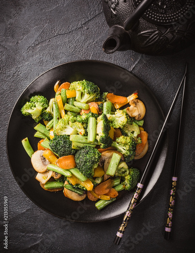 Top view of hot stir fried vegetables on black plate. Healthy asian food concept with copy space. Toned photo.