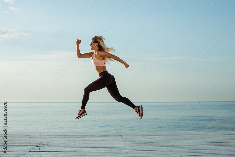 Young woman with fit body jumping and running against blue sea Young woman with fit body jumping and running against blue sea