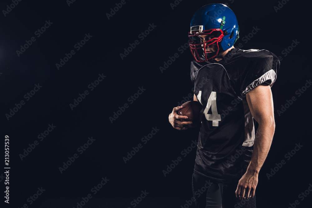 american football player in black uniform with ball in hand isolated on black american football player in black uniform with ball in hand isolated on black