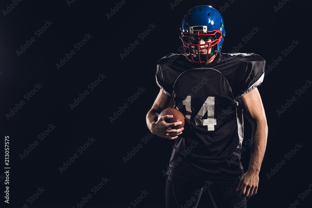 young american football player with ball looking at camera isolated on black