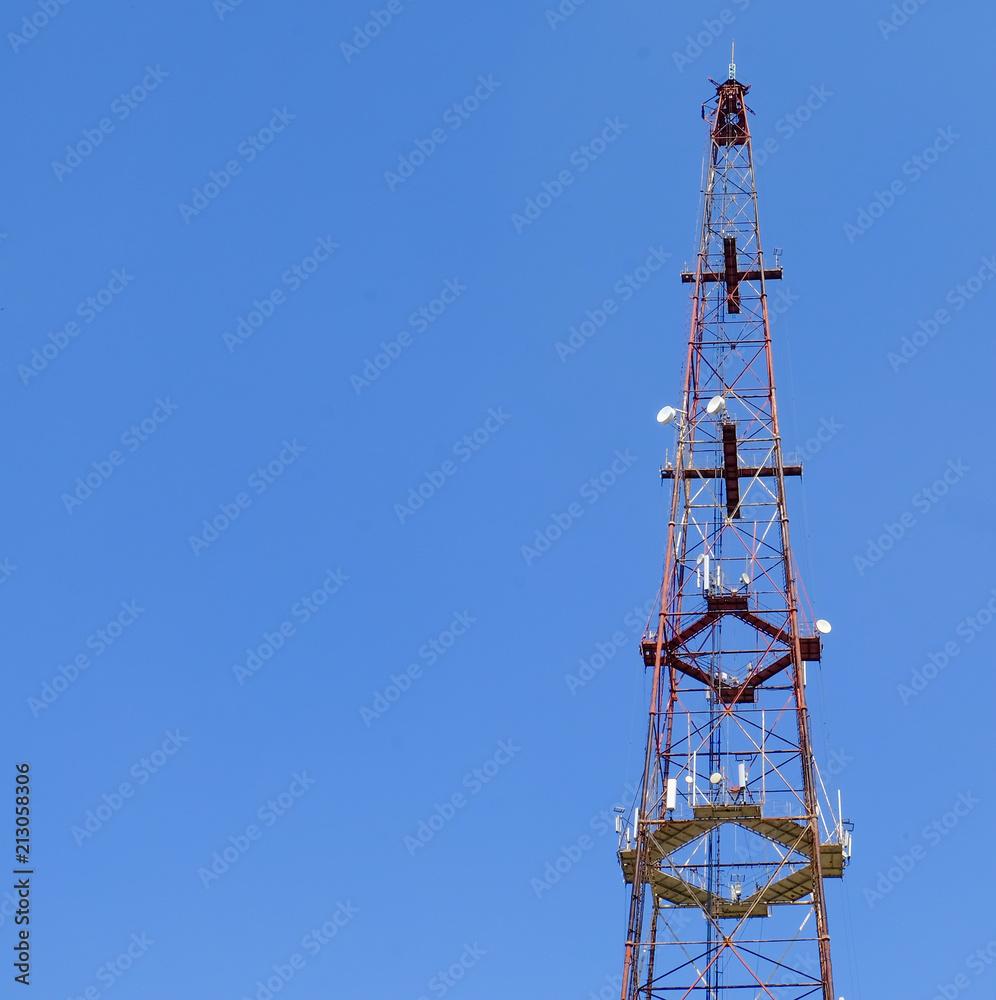 Telecommunication tower include of radio microwave and television antenna system with cloud blue sky and sun ray. Antenna tower, low angle view.