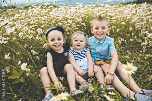 three cute childs playing in green daisy field photo