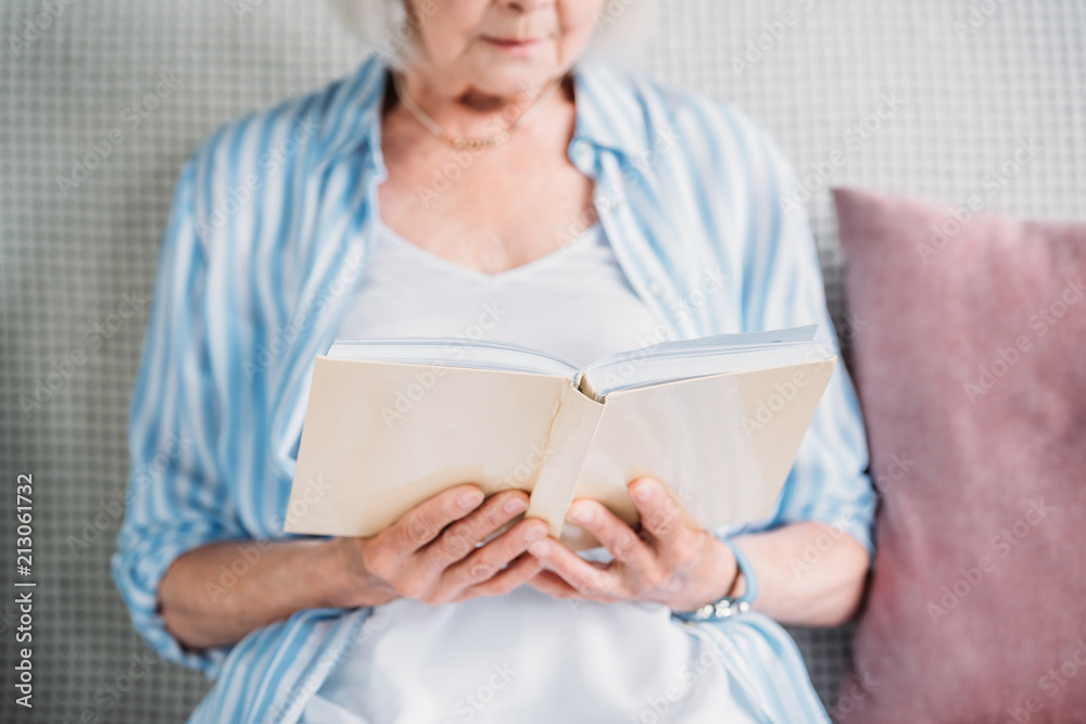 cropped shot of senior woman reading book while resting on sofa at home cropped shot of senior woman reading book while resting on sofa at home