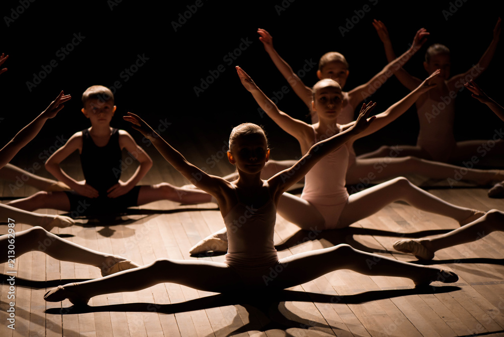 Obraz premium Pretty young girl and boy sitting on stage having stretching and training for ballet dances.