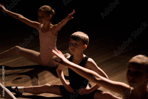 Pretty young girl and boy sitting on stage having stretching and training for ballet dances.
