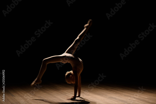 Flexible child, beautiful little gymnast girl doing gymnastic exercises, black background. Sport, training, stretching, active lifestyle concept.