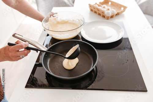 Cropped photo of woman cooking in kitchen at home, and frying pancakes on modern stove