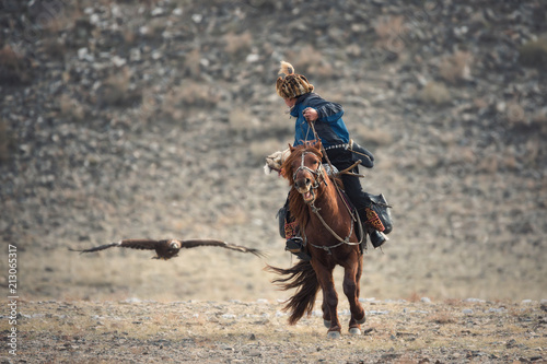 Falconry In Western Mongolia,Golden Eagle Festival.Artistic Scene From The Life Of The Nomadic Peoples Of Asia: Rider On Brown Horse And And The Flying Golden Eagle. Mongolian Nomad On Horseback