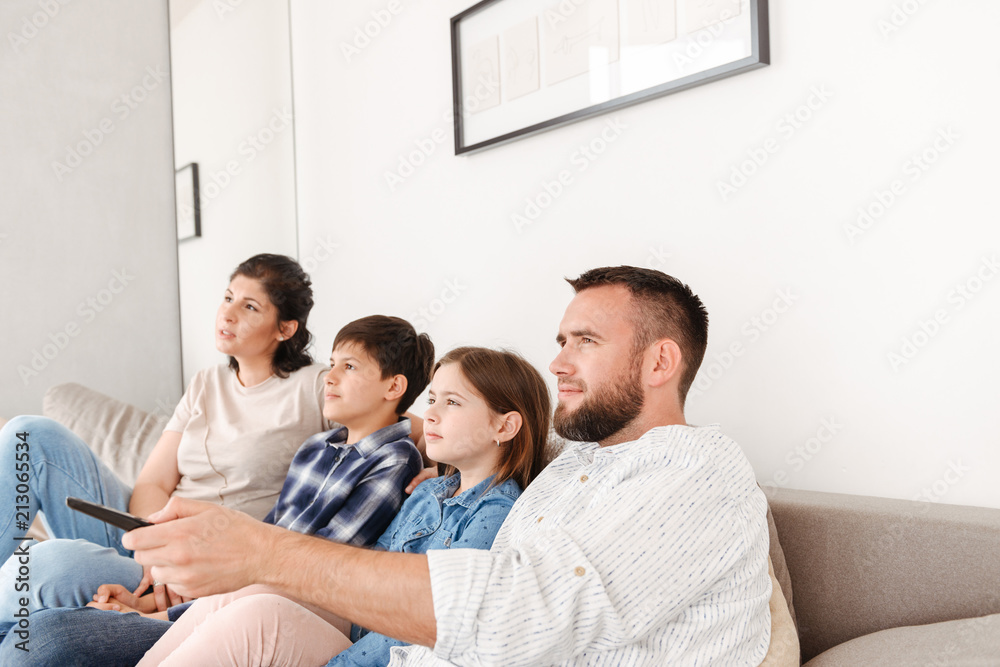 Portrait of happy family with two children resting in living room at home, and sitting on sofa together while watching tv Portrait of happy family with two children resting in living room at home, and sitting on sofa together while watching tv