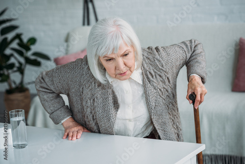 portrait of grey hair woman with walking stick trying to get up at home photo