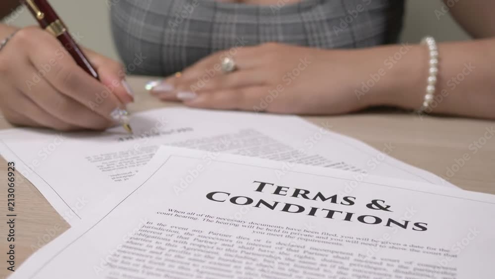 Terms and conditions legal document being signed by a woman sitting at a desk. Terms and conditions legal document being signed by a woman sitting at a desk.