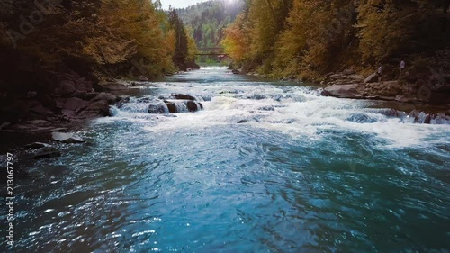 Low flight over the mountain river, blue in the middle of the forest and mountains. Sunset time. The sun's rays give orange flare. The concept of curing urological diseases and prostatitis.