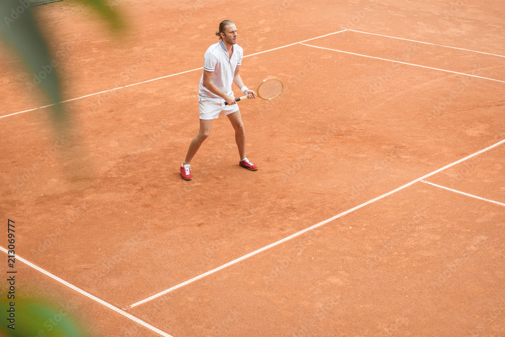 old-fashioned tennis player training with racket on brown tennis court