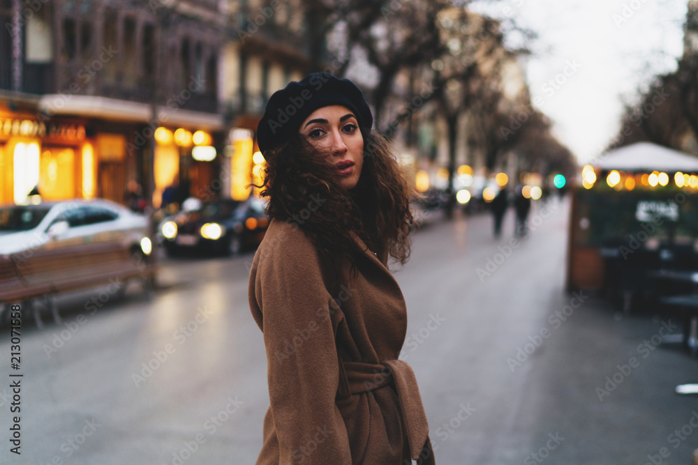 Fototapeta premium Successful business woman enjoying vacation in a small european city in the autumn time. Beautiful student girl wearing stylish clothes crossing road while going home at the evening.