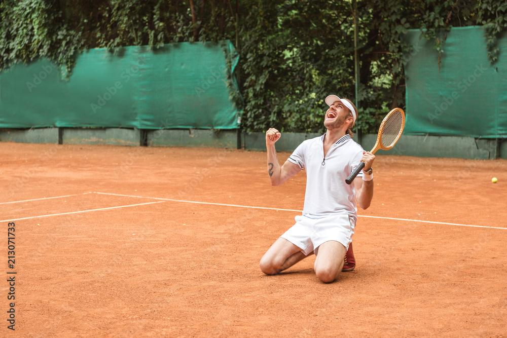 blond winner with racket celebrating and kneeling on tennis court
