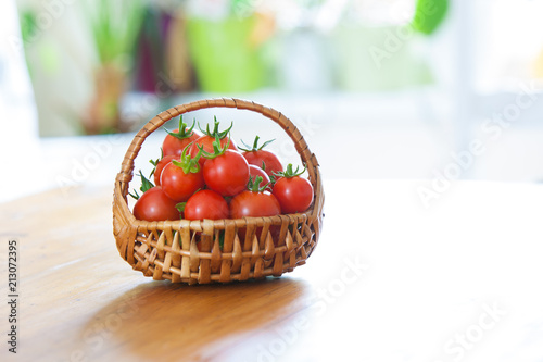 Fototapeta Naklejka Na Ścianę i Meble -  basket full of tomatoes in front of a green yellow blurry background on a wooden table