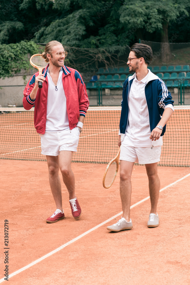cheerful sportive friends with wooden rackets walking on tennis court