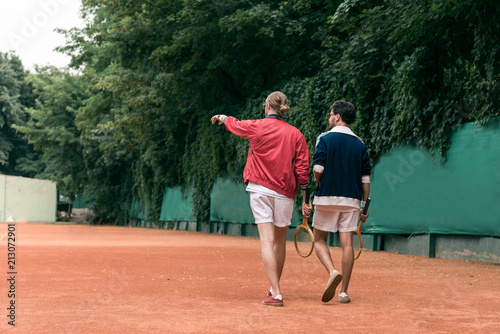 back view of retro styled friends with wooden rackets walking on tennis court