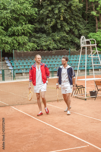 old-fashionedfriends with wooden rackets walking on tennis court