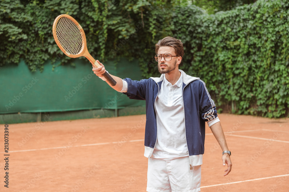 handsome tennis player pointing with wooden racket on tennis court