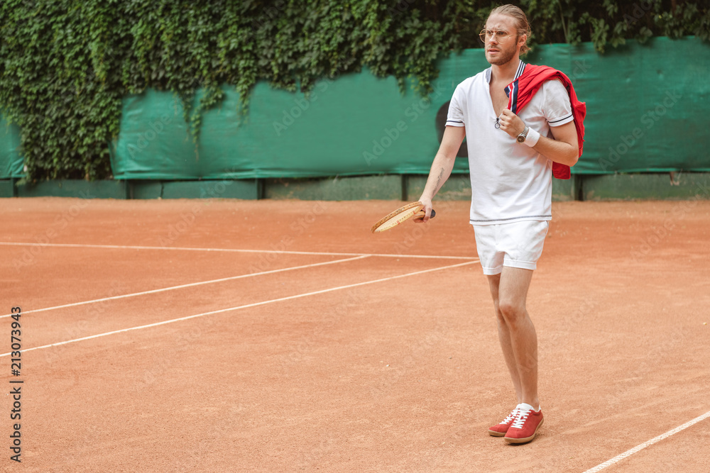 handsome man in sportswear with retro wooden racket on tennis court