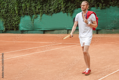 handsome man in sportswear with retro wooden racket on tennis court