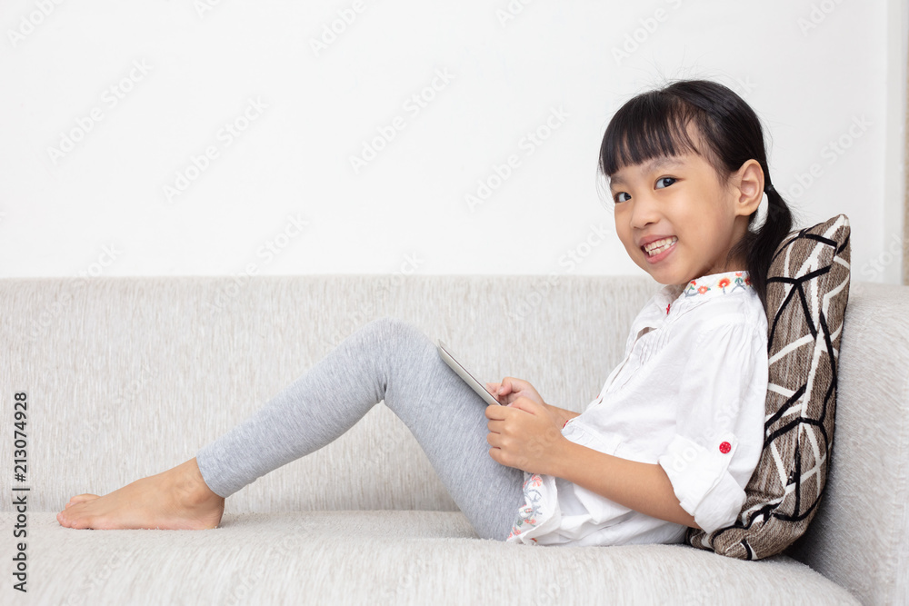 Asian Chinese little girl sitting on the sofa playing digital tablet Asian Chinese little girl sitting on the sofa playing digital tablet