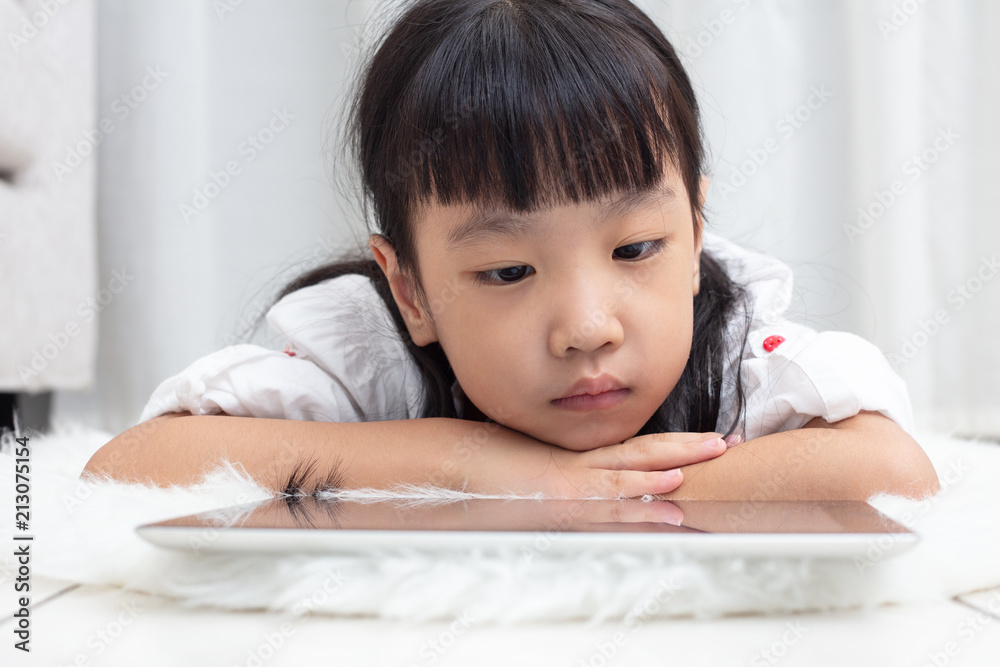 Asian Chinese little girl lying on the floor and playing tablet Asian Chinese little girl lying on the floor and playing tablet
