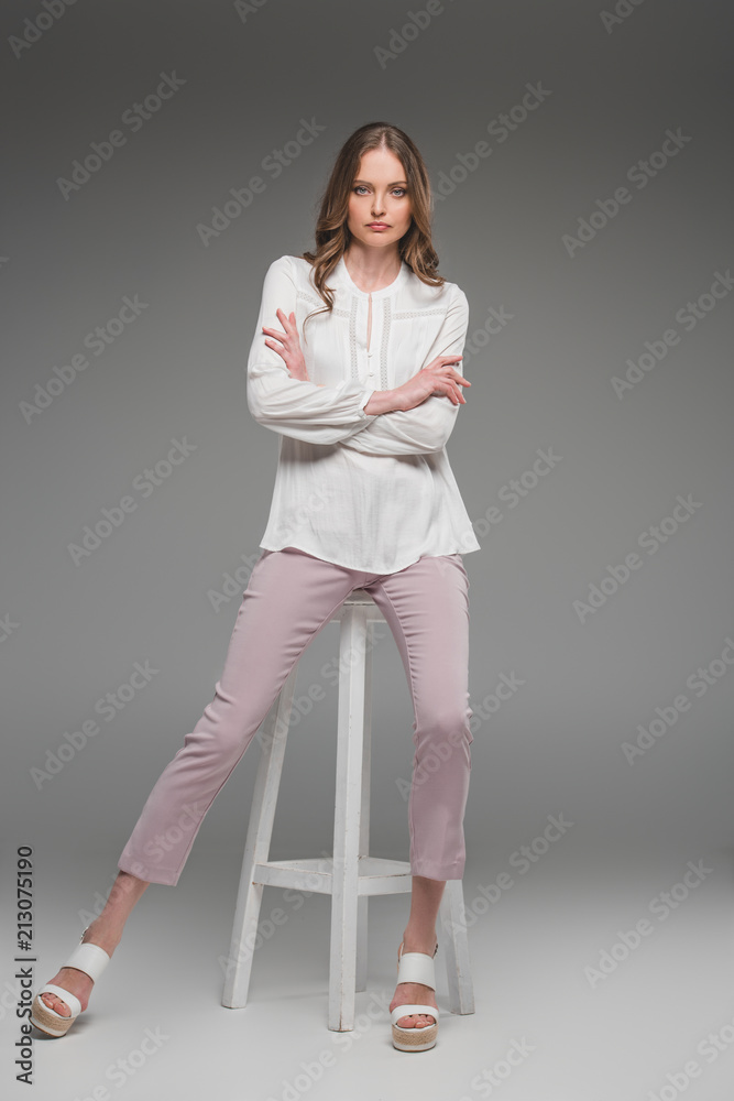 serious attractive woman with folded arms sitting on chair on grey background serious attractive woman with folded arms sitting on chair on grey background
