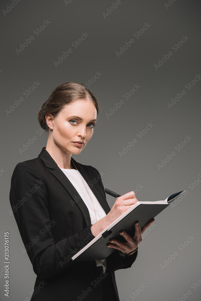 attractive businesswoman writing in textbook isolated on grey background attractive businesswoman writing in textbook isolated on grey background