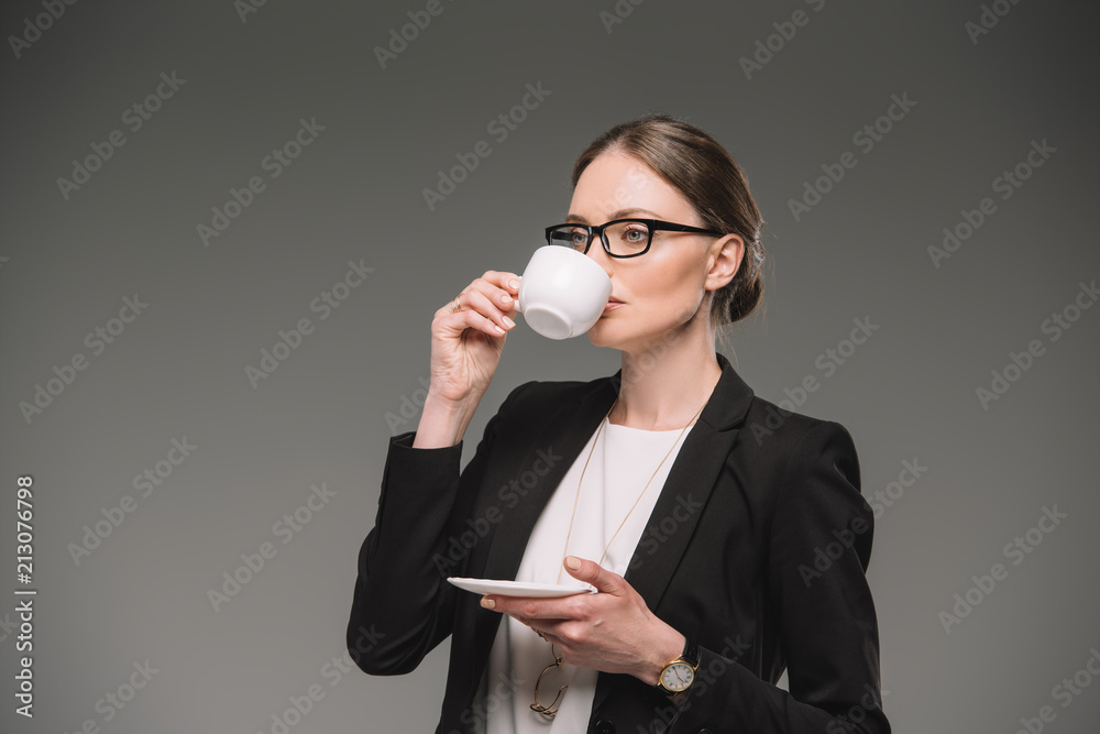businesswoman in eyeglasses drinking coffee from cup isolated on grey background businesswoman in eyeglasses drinking coffee from cup isolated on grey background