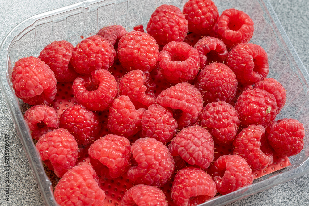Friche reife geerntete Himbeeren in einer durchsichtigen Plastikschale aus dem Supermarkt Friche reife geerntete Himbeeren in einer durchsichtigen Plastikschale aus dem Supermarkt