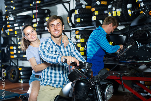 couple sitting on new motorbike in workshop.