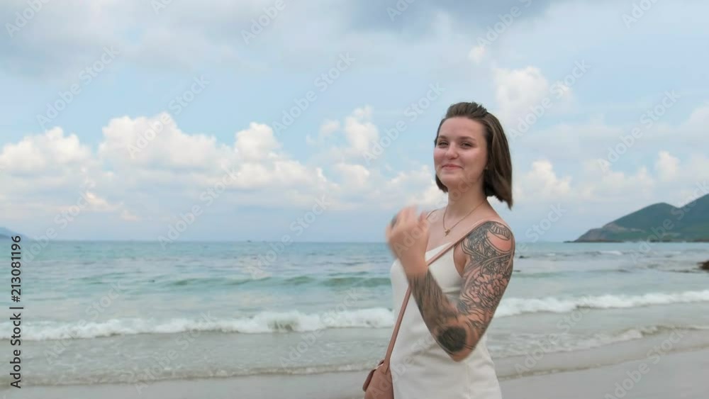 A beautiful smiling woman is walking by the ocean shore and playing with her hair A beautiful smiling woman is walking by the ocean shore and playing with her hair