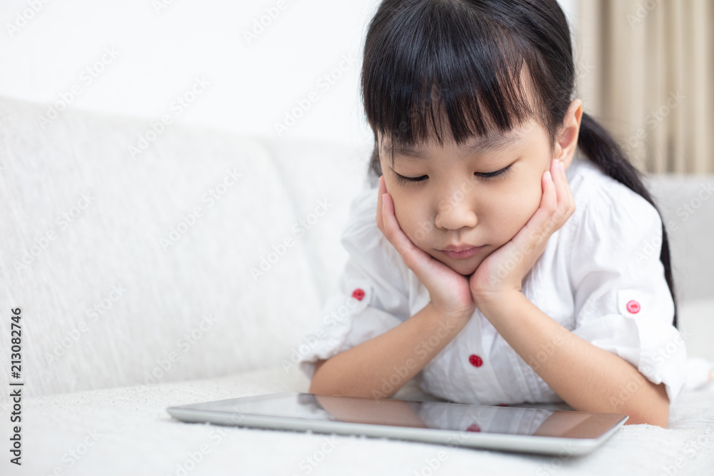 Asian Chinese little girl lying on the sofa and playing tablet Asian Chinese little girl lying on the sofa and playing tablet