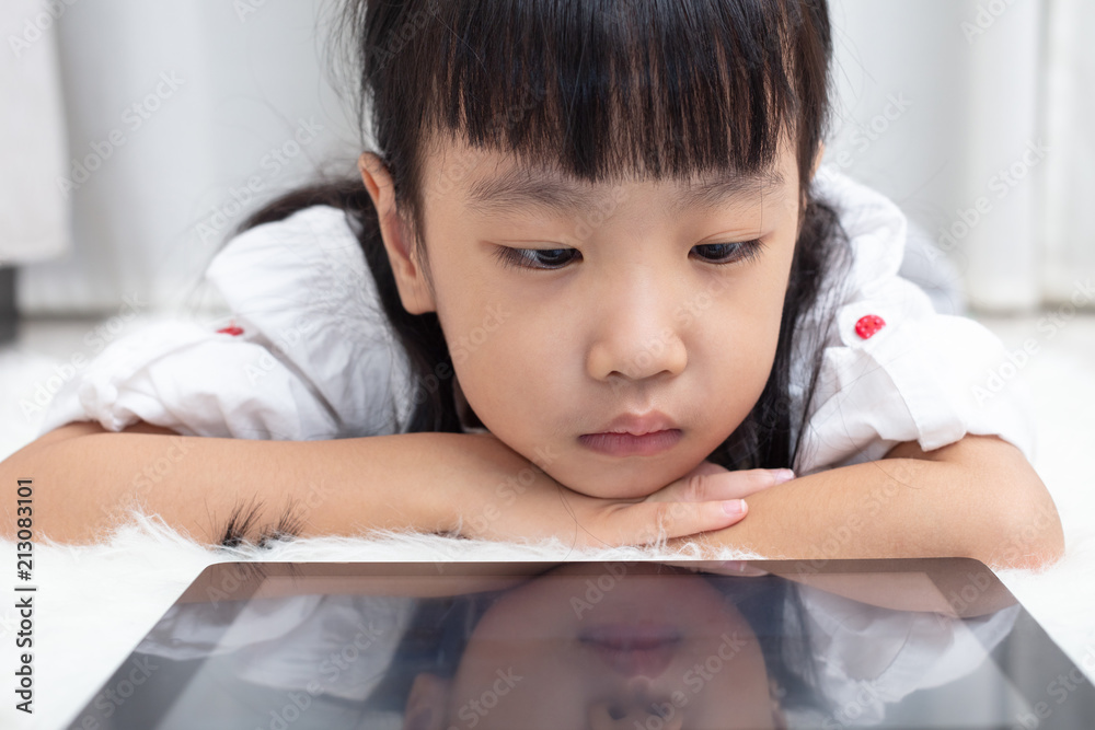 Asian Chinese little girl lying on the floor and playing tablet Asian Chinese little girl lying on the floor and playing tablet