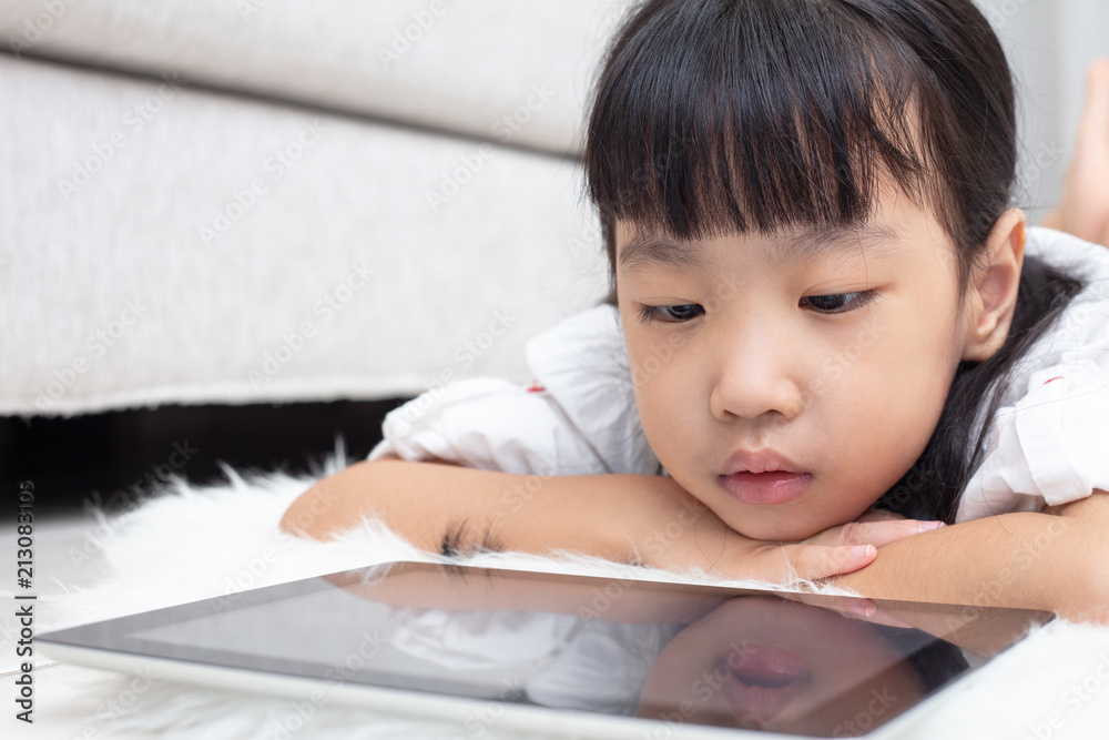 Asian Chinese little girl lying on the floor and playing tablet Asian Chinese little girl lying on the floor and playing tablet