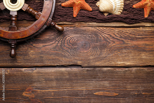 Ship's steering wheel, shells and brown fishing net on wooden table