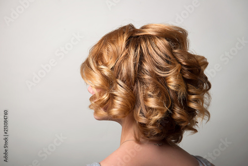 Hairstyle short curls on the head of the blonde back view of the head turning left. A woman's hairdo.