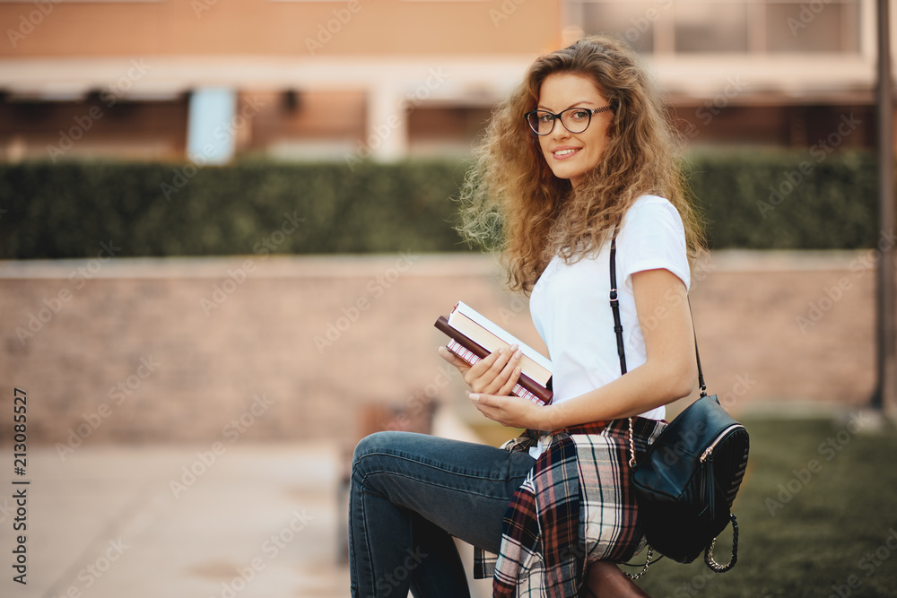 Obraz premium Female student sitting in a campus and waiting for class to begin. Books in hands.